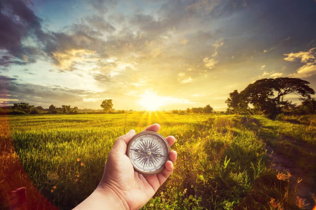 A man holding compass on hand at field and sunset for navigation guide.