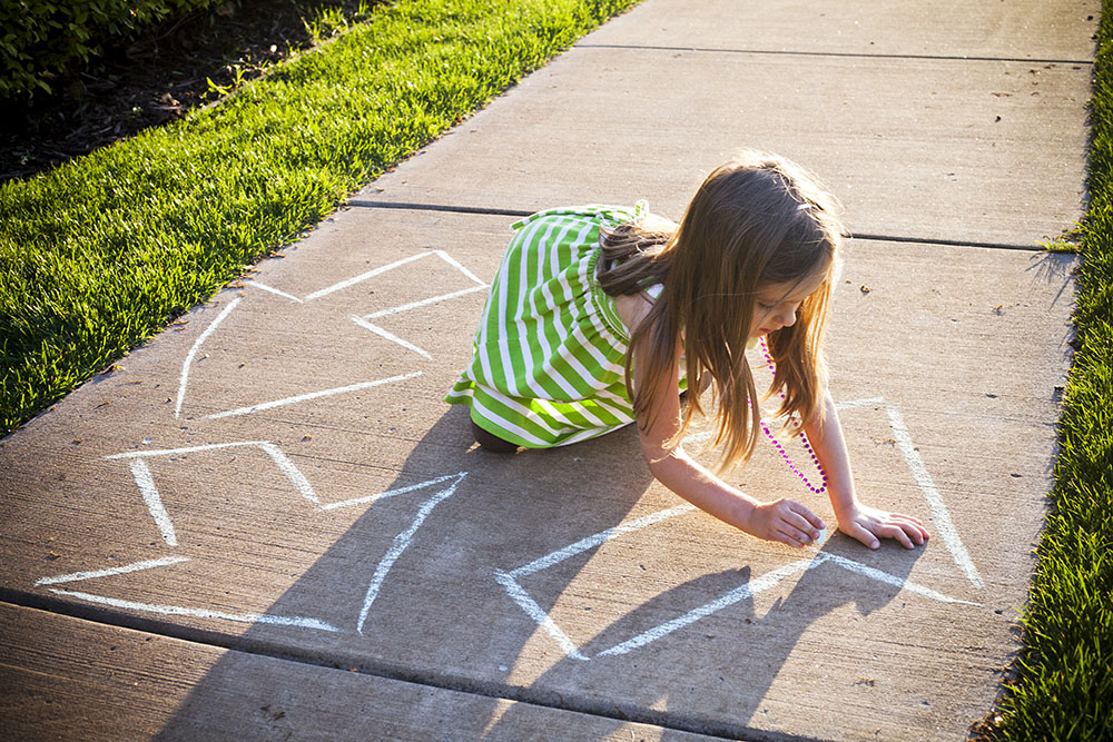 a young girl writes a recycling symbol on the sidewalk