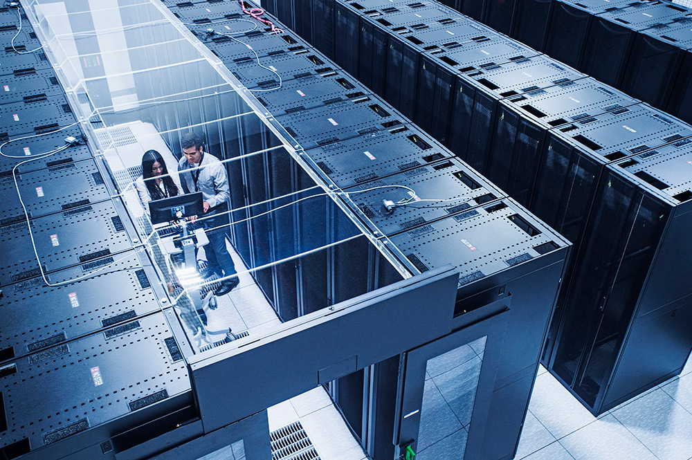 High-angle view of a server room with two technicians working among data center racks